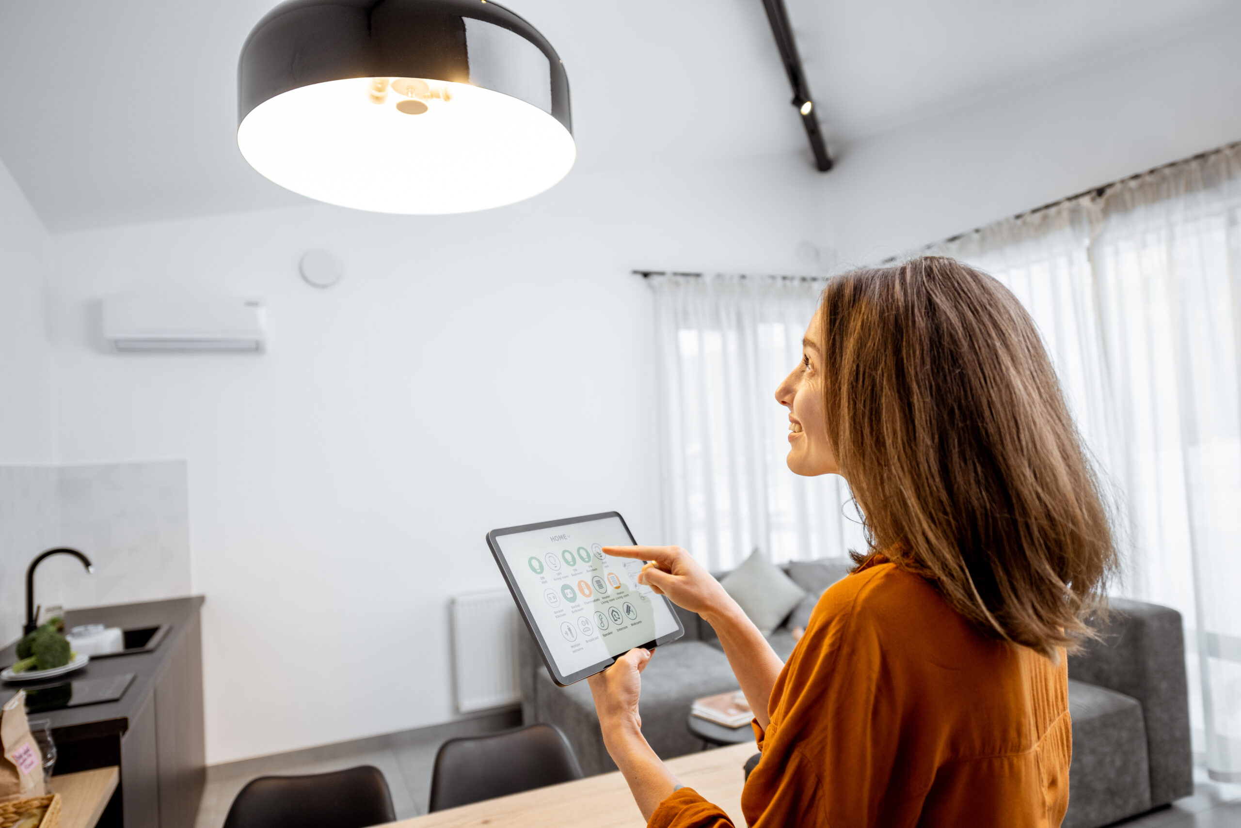 Young woman controlling home light with a digital tablet in the living room. Concept of a smart home and light control with mobile devices